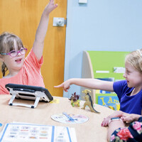 A bunch of kids sitting around a table with a device on the table